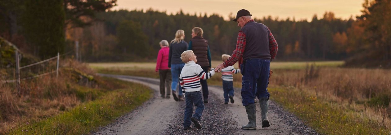 Familj i tre generationer går på en grusväg i solnedgången.