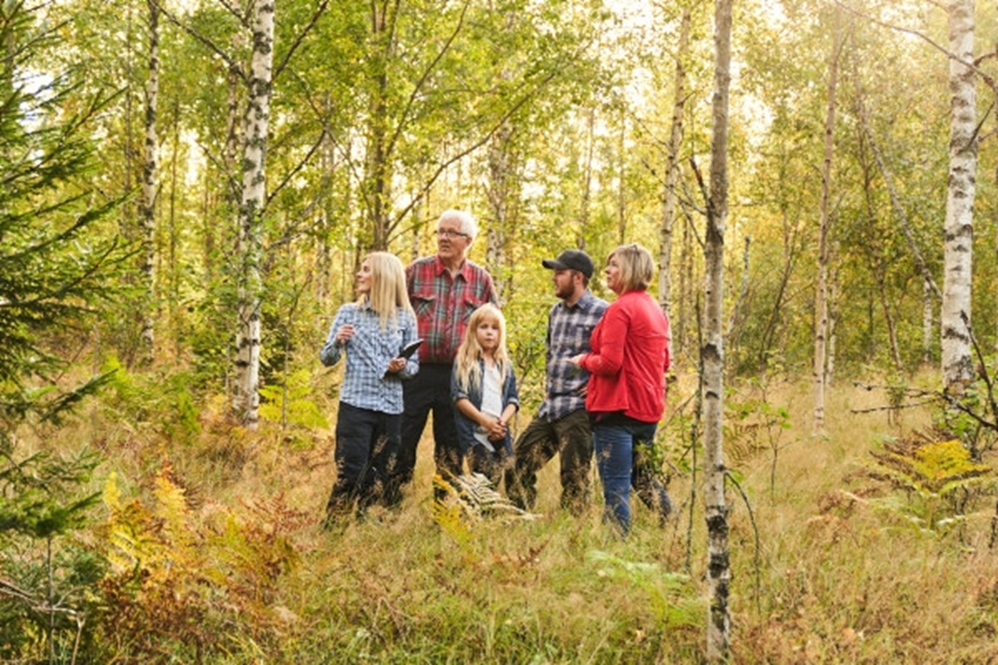 En grupp människor i olika åldrar står i en blandskog.